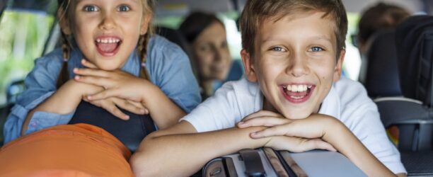 bambini sorridenti in auto appoggiati alle valigie